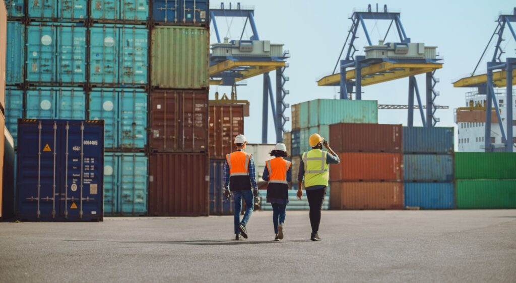 Workers walking through a shipping cargo container terminal depot.