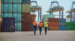 Workers walking through a shipping cargo container terminal depot.