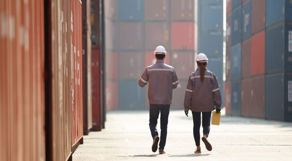 Two workers walking between shopping containers.