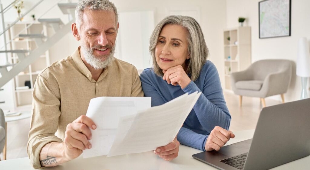 A senior couple sit at a laptop comparing multiple documents