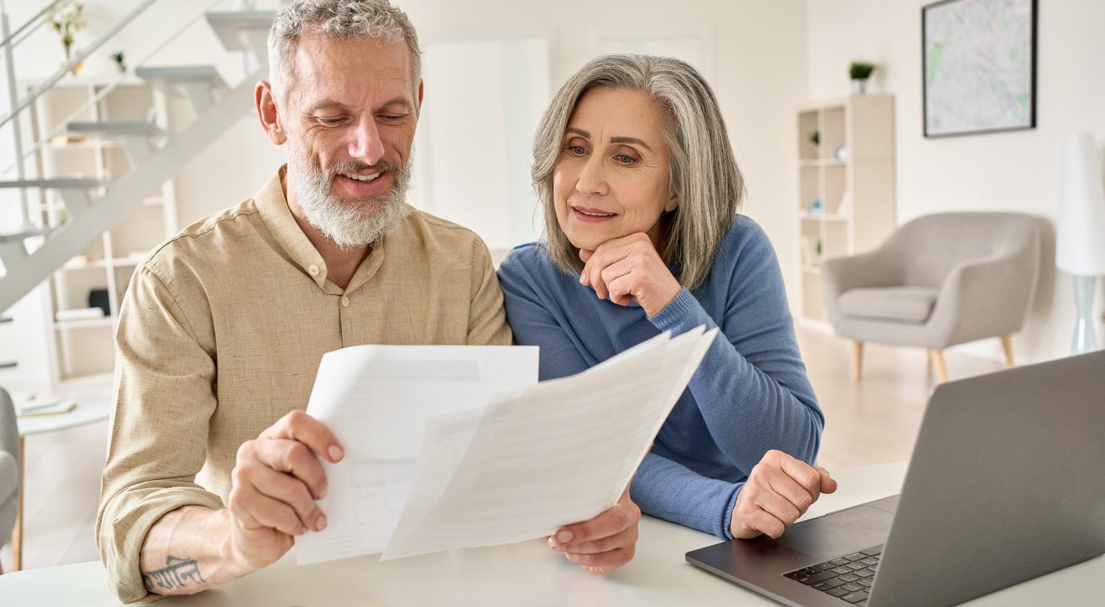 A senior couple sit at a laptop comparing multiple documents