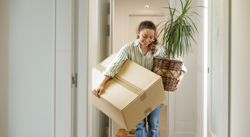 A woman carrying a box and a plant into her new home.