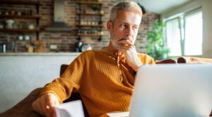 A man in his 50s thinking while using a laptop